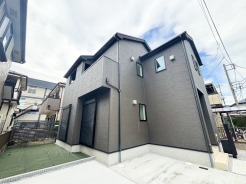 外壁は濃いグレーで、窓にはシャッターが設置されている住宅です。